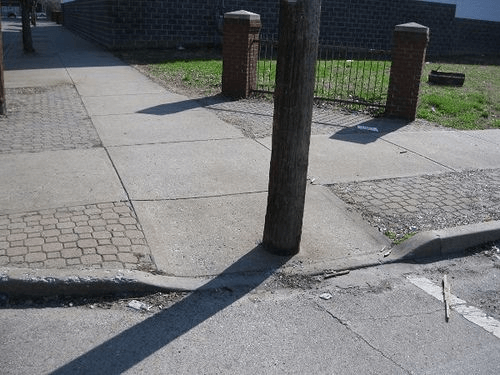 Crosswalk curb cut with telephone pole directly in the middle of the sidewalk blocking the path